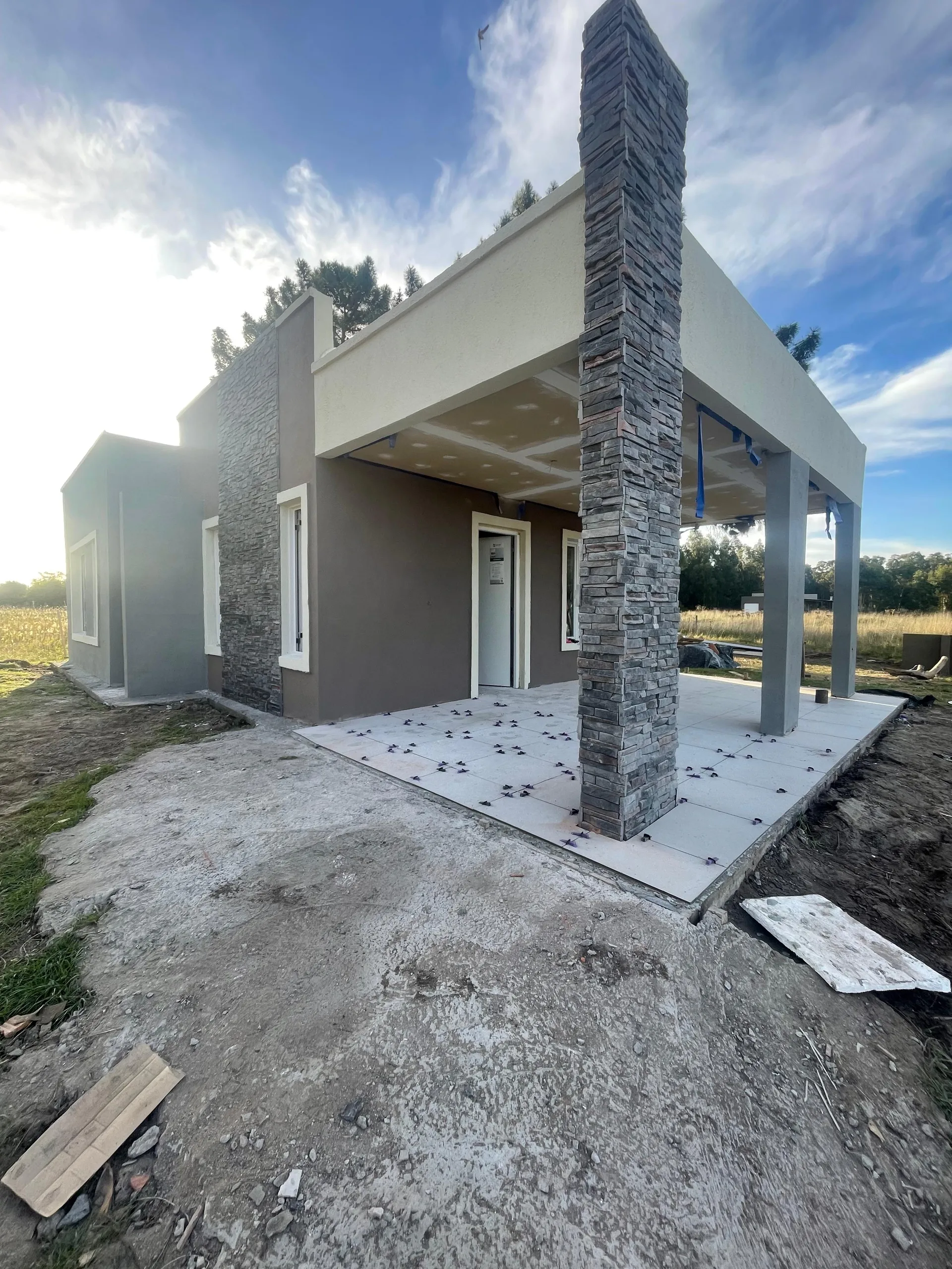 Vivienda terminada de día, con la columna revestida en piedra en primer plano